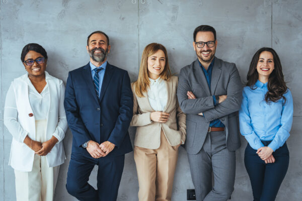 white collar professionals lined up along a wall and smiling