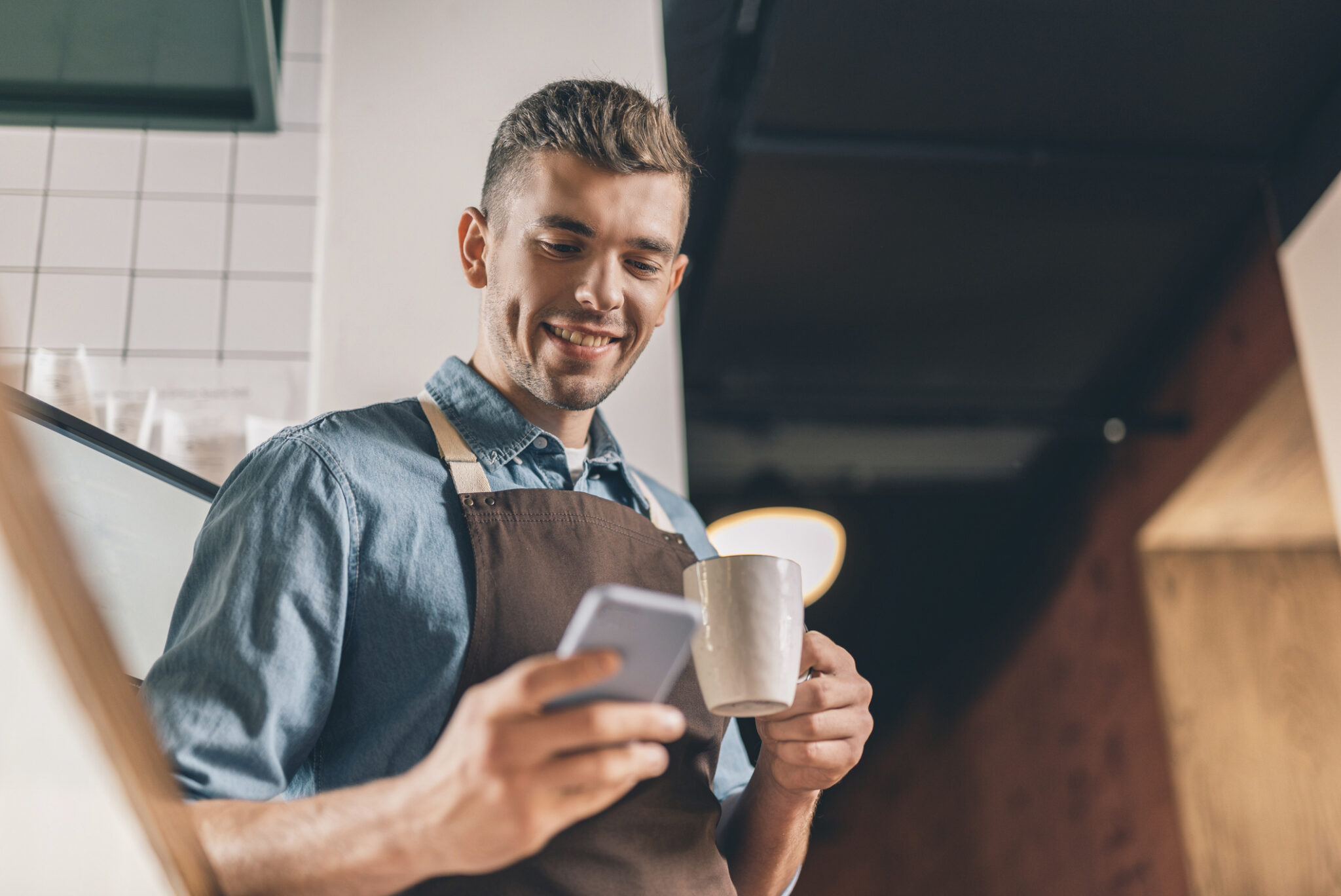 cafe employee smiling looking at phone with coffee mug