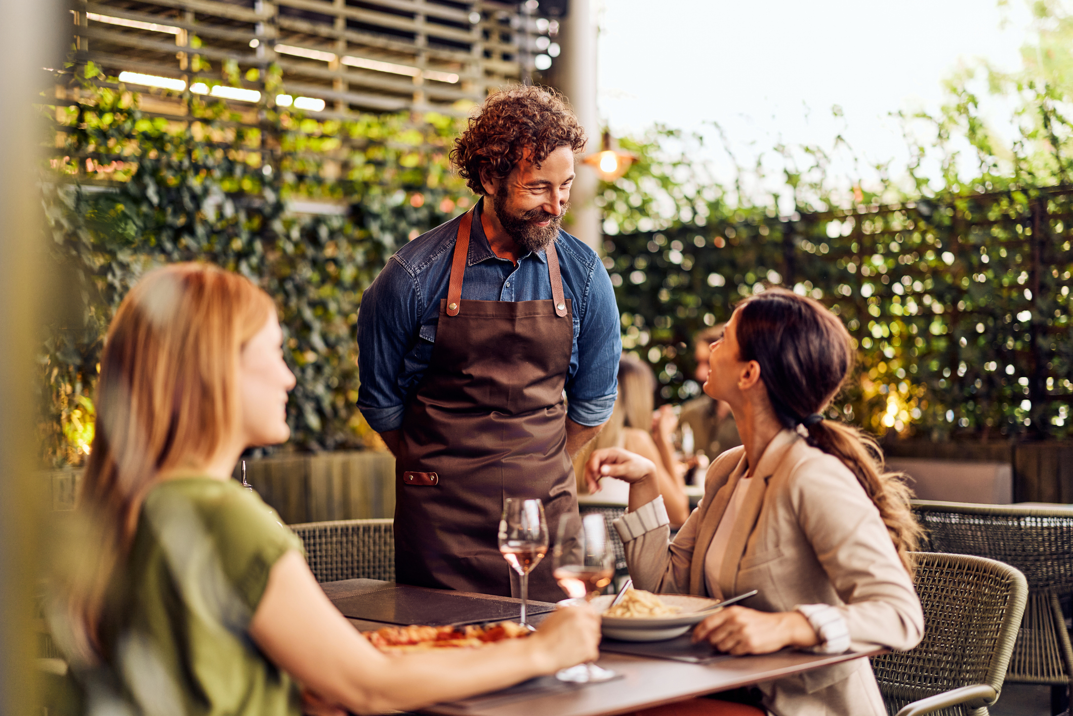 A table server talking to diners at an outdoor restaurant.